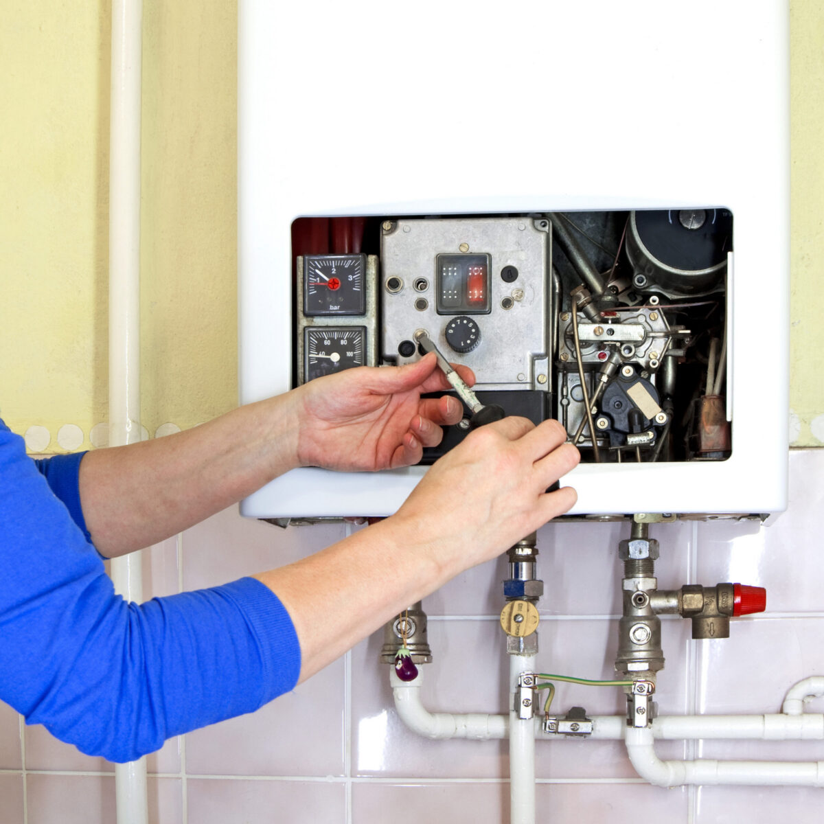 Technician performing tankless water heater repair on unit with exposed components and pipes